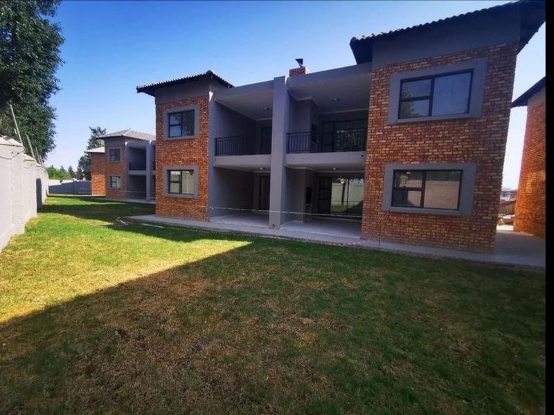 Rear view of a modern apartment complex featuring exposed brick facades, covered ground-floor patios, upper-level balconies, and a well-maintained communal lawn area.