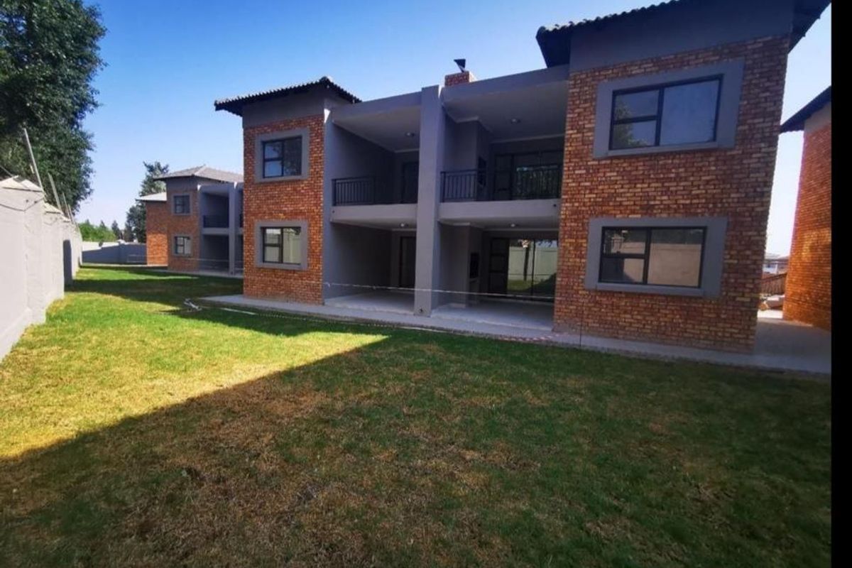 Rear view of a modern apartment complex featuring exposed brick facades, covered ground-floor patios, upper-level balconies, and a well-maintained communal lawn area.