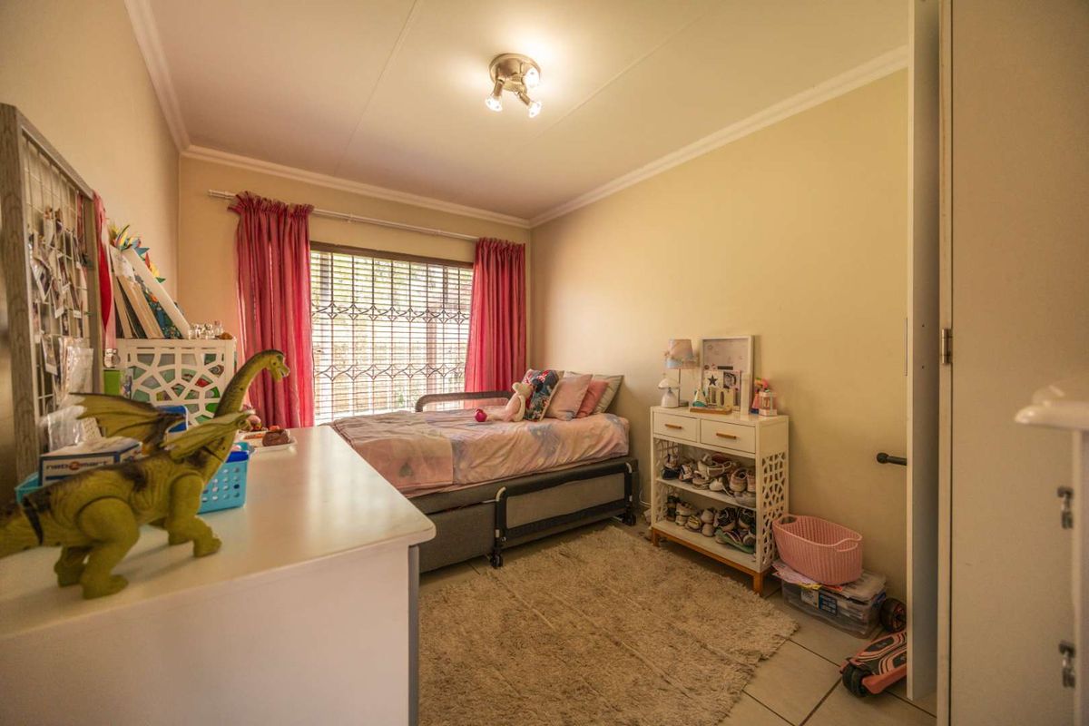 A functional bedroom featuring tiled flooring, a security gate on the window, and a built-in cupboard, providing a practical living space.