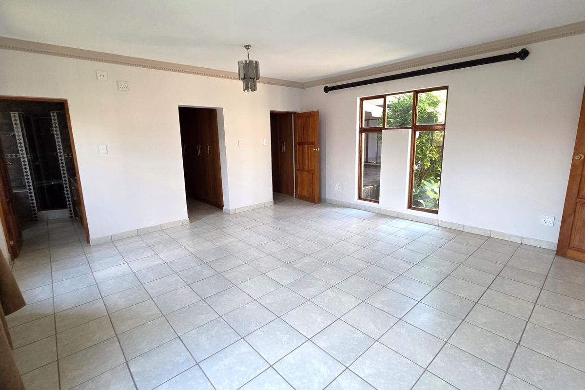 Spacious bedroom featuring neutral tiled flooring, built-in wooden cupboards, and large windows providing natural light and garden views.