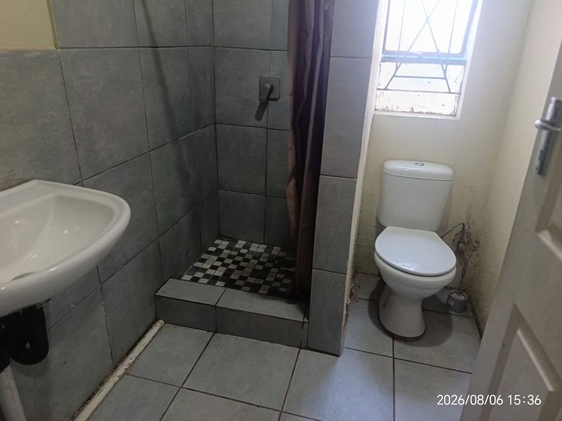A functional bathroom featuring a shower, pedestal basin, and toilet with tiled finishes. The space requires minor maintenance and cosmetic updates.