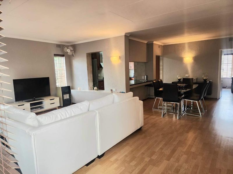 Spacious open-plan living and dining area featuring laminate flooring, wall-mounted lighting, and a convenient pass-through window connecting to the kitchen.