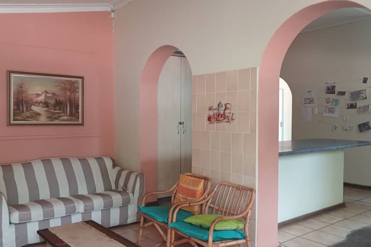 A living area featuring distinctive arched doorways leading to an adjacent kitchen space with a breakfast counter and tiled flooring.