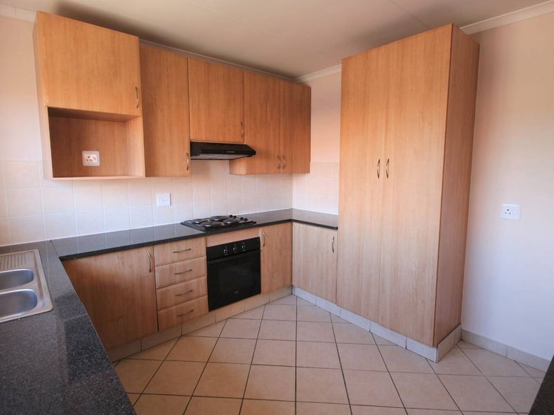 A functional kitchen featuring light wood-finish cabinetry, dark countertops, built-in oven, gas hob, and tiled flooring.