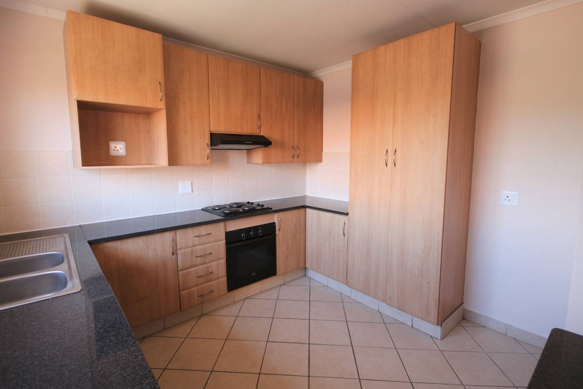A functional kitchen featuring light wood-finish cabinetry, dark countertops, built-in oven, gas hob, and tiled flooring.