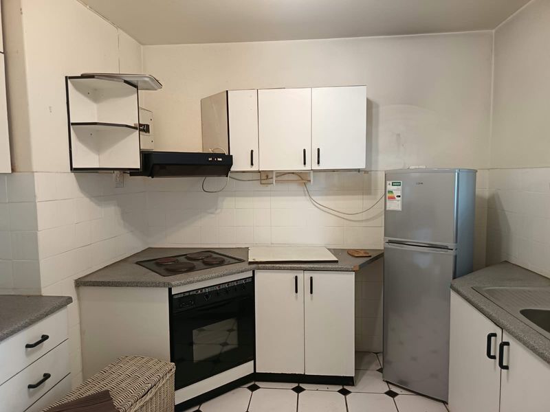 A compact kitchen featuring white cabinetry, a built-in oven with electric hob, tiled backsplash, and functional laminate countertops.