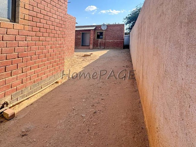 A side or rear exterior passage featuring exposed brick and plastered boundary walls with an unpaved ground surface.