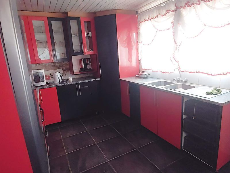 A functional kitchen featuring high-contrast red and black cabinetry, laminate countertops, a double basin sink, and tiled flooring.