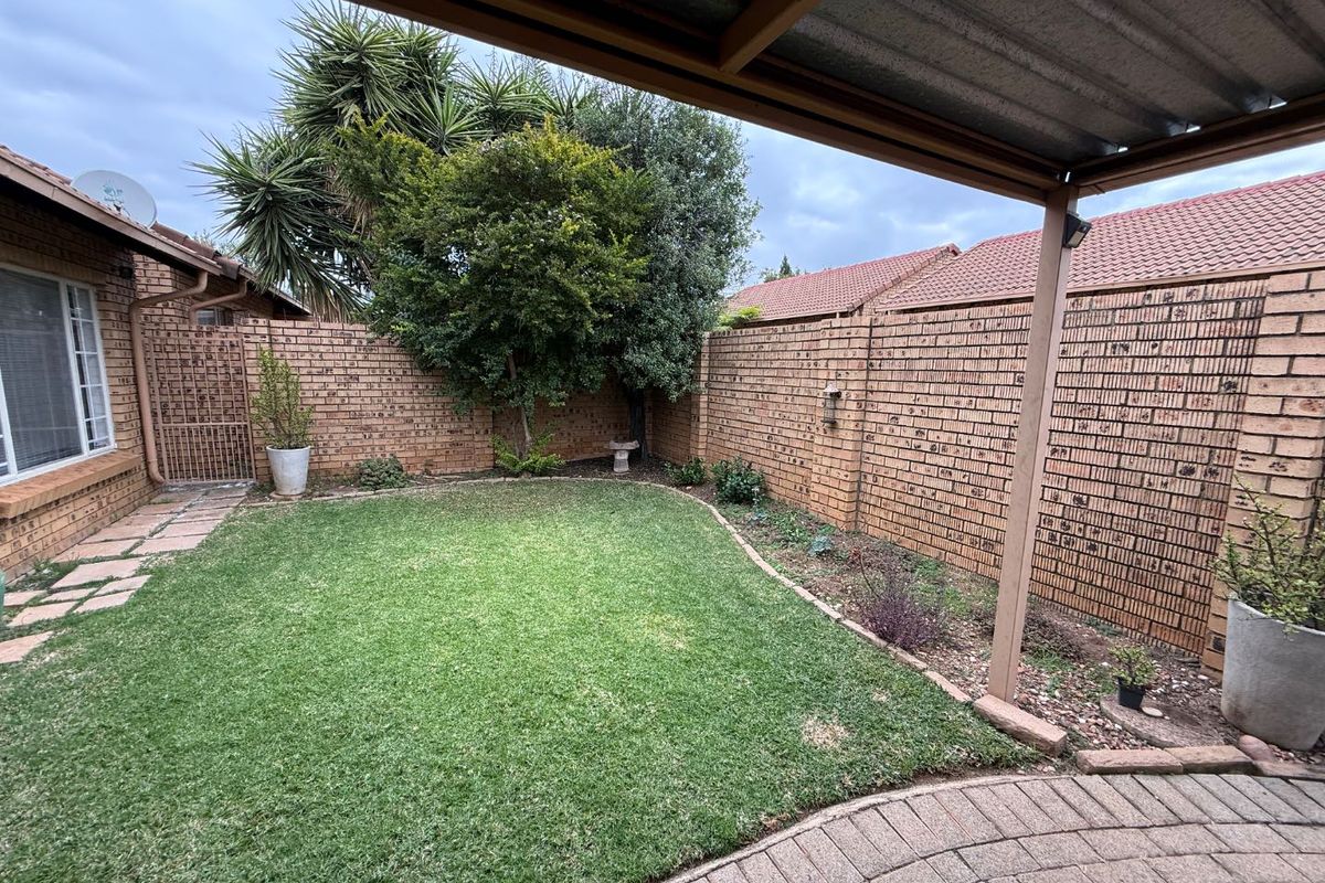 A private rear garden featuring a paved patio area under a covered structure, enclosed by brick boundary walls and established greenery.
