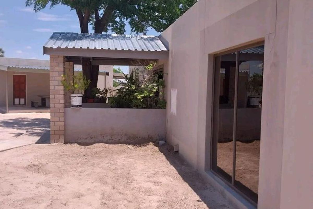 Exterior view of the property featuring a covered patio area, sliding glass doors, and an unfinished sandy yard.