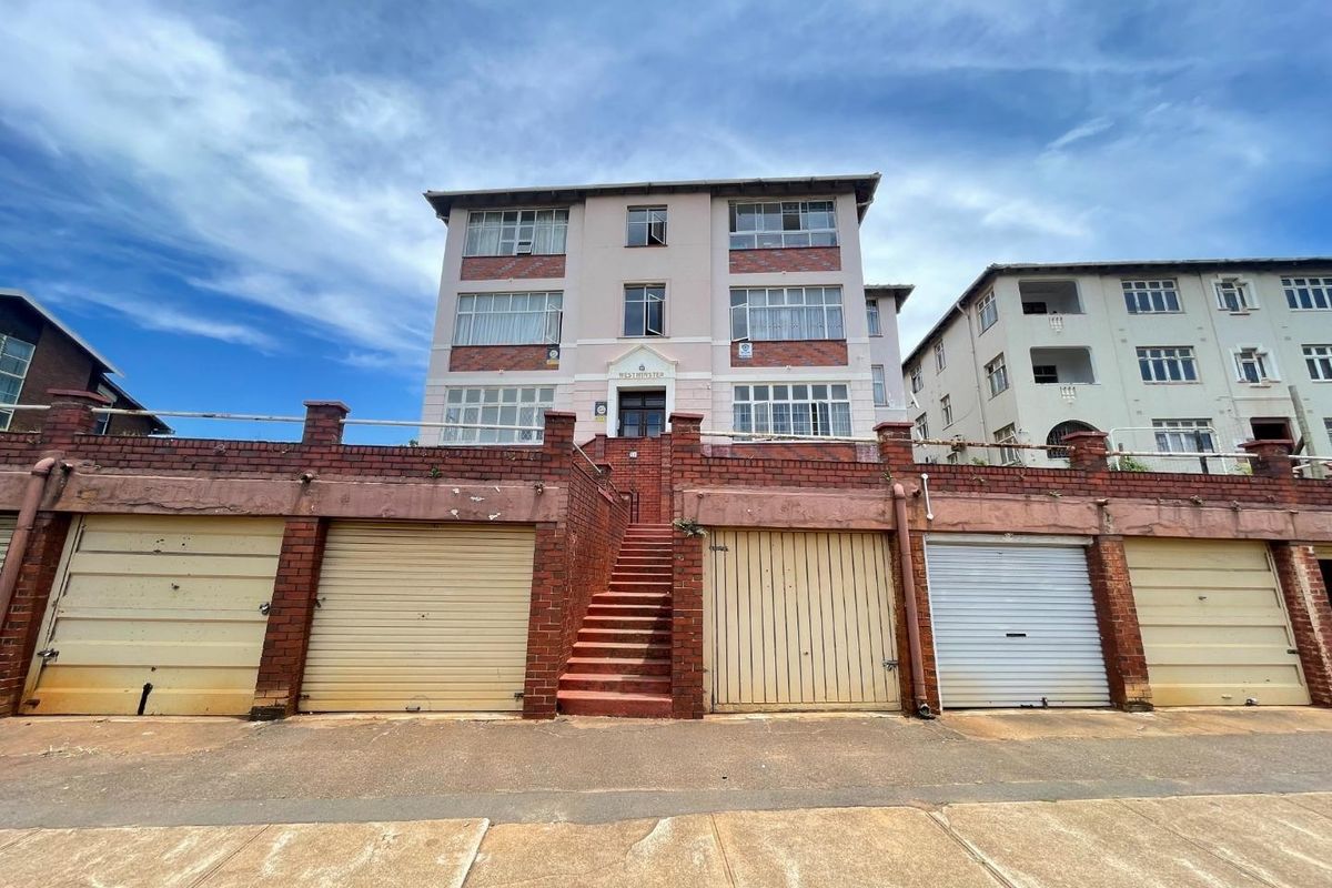 Front elevation of a multi-story apartment building featuring a brick retaining wall, multiple garage units, and a central staircase entrance.