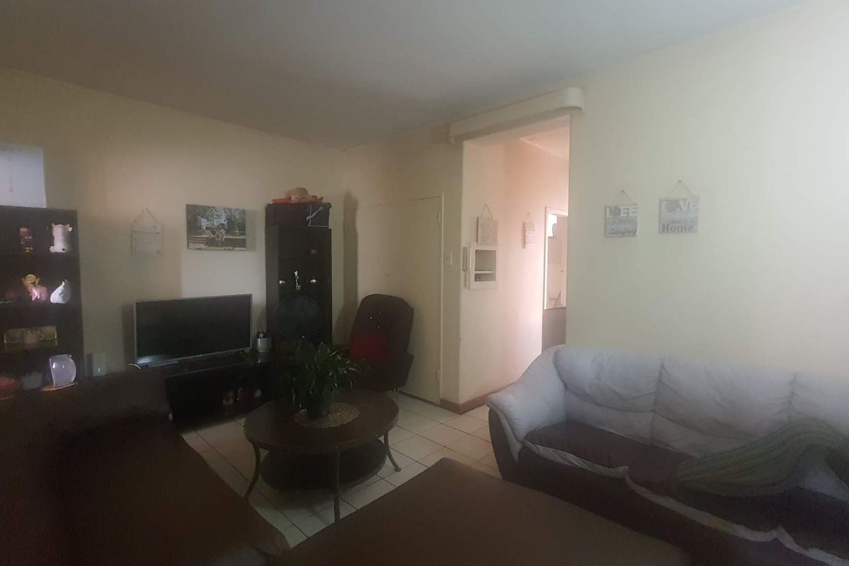A living room area featuring tiled flooring and access to an adjacent hallway, providing a functional space for relaxation.