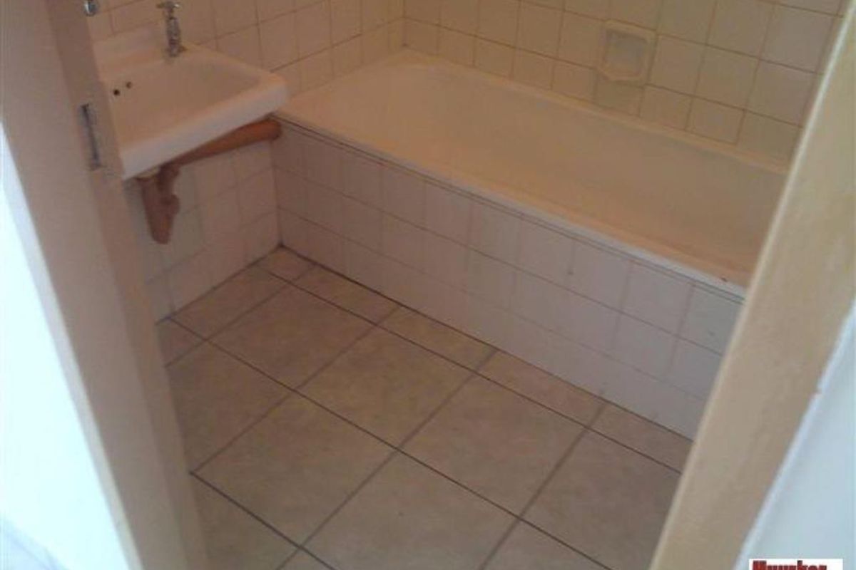 A compact bathroom featuring a standard bathtub, wall-mounted basin, and tiled finishes throughout.