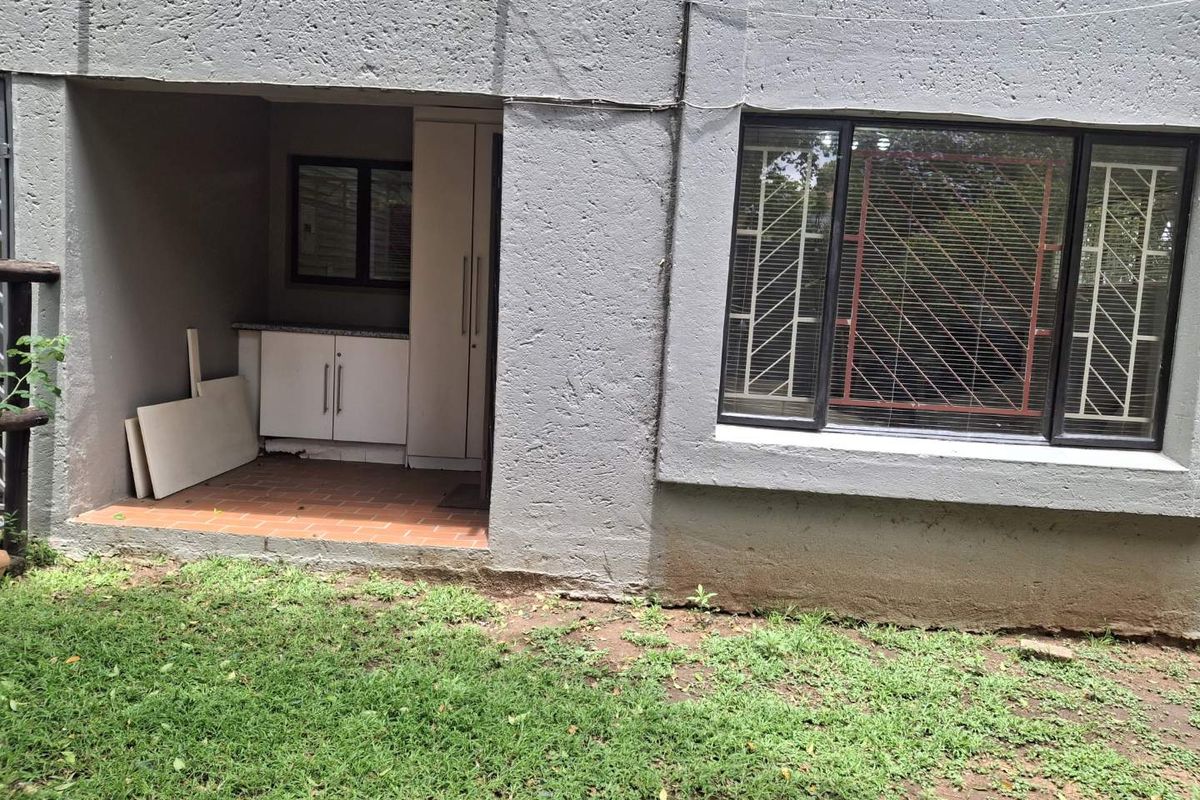 Rear exterior view of an apartment featuring a small covered patio area with built-in cabinetry and a granite countertop, adjacent to a garden space.