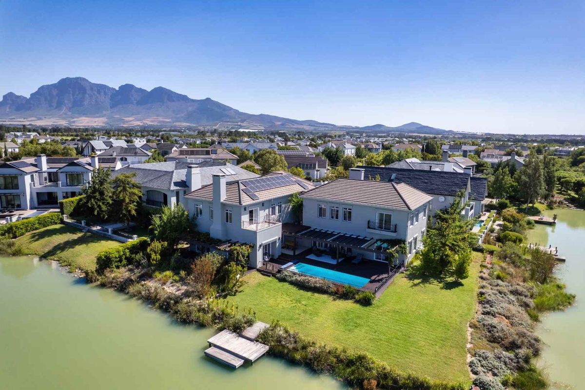 Aerial view of a luxury waterfront residence featuring a swimming pool, timber deck, pergola, and private jetty, set against a scenic mountain backdrop.