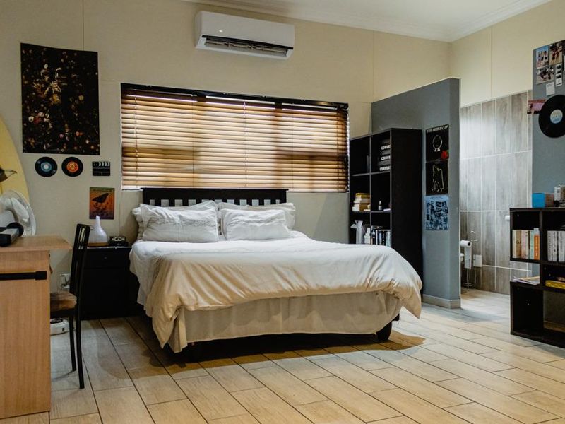 A bedroom featuring tiled flooring, a wall-mounted air conditioning unit, and an open-plan layout with an adjacent tiled bathroom area.