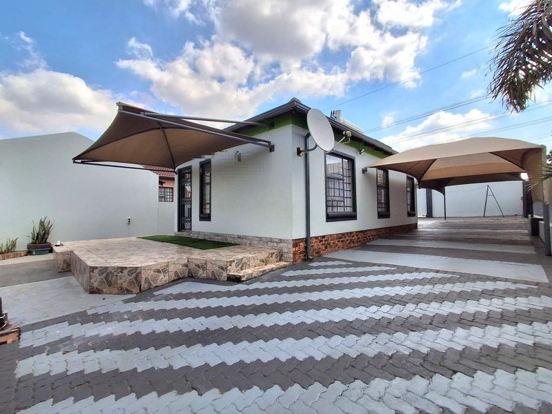 Front exterior view featuring a paved driveway, carport, tiled patio area with a retractable awning, and secure window bars.