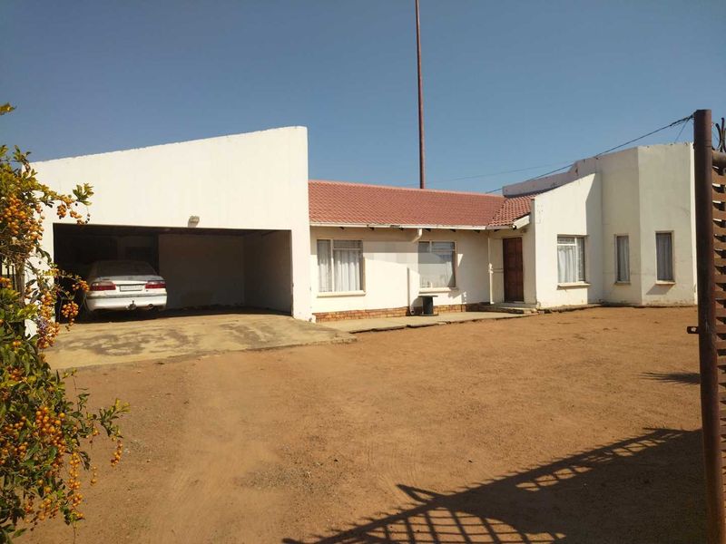 Front exterior view of a single-story house featuring a tiled roof, attached garage, and an unpaved yard area.