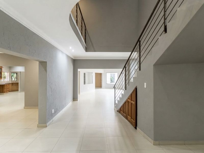 Spacious open-plan living area featuring neutral tiled flooring, a modern staircase with metal balustrades, and convenient under-stair storage.