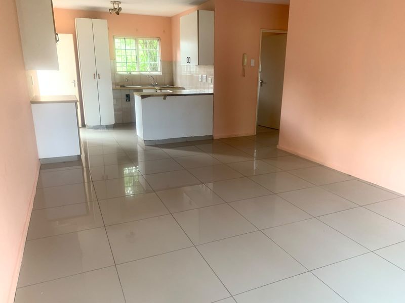 An open-plan living and kitchen area featuring neutral tiled flooring, built-in cabinetry, and a functional kitchen layout in a vacant apartment setting.