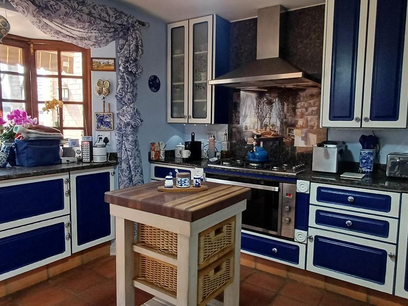 A traditional kitchen featuring blue and white cabinetry, stone countertops, a gas hob with extractor fan, and terracotta floor tiles.