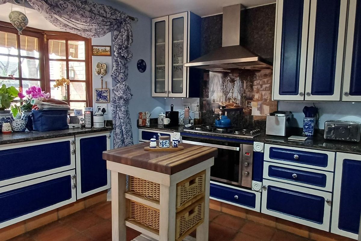 A traditional kitchen featuring blue and white cabinetry, stone countertops, a gas hob with extractor fan, and terracotta floor tiles.