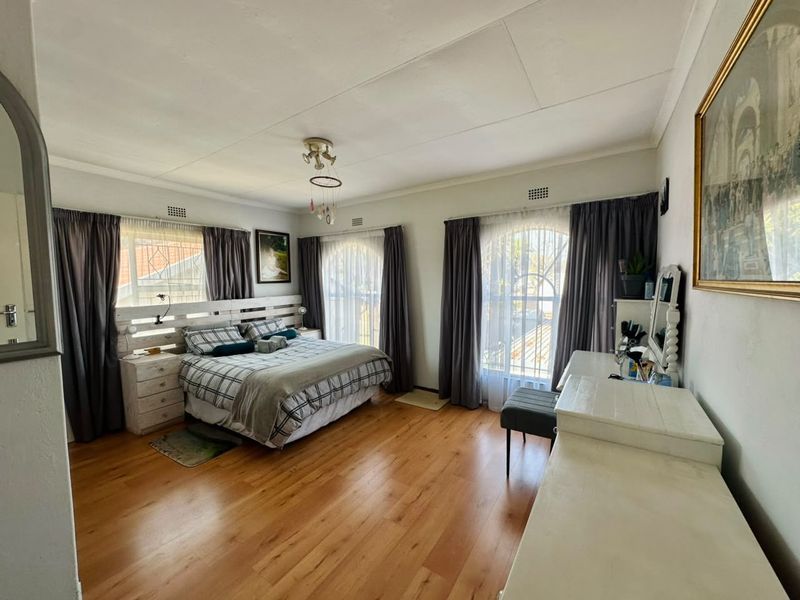 Spacious bedroom featuring warm laminate flooring, dual arched windows with curtains, and functional ceiling ventilation, offering a comfortable and well-lit living space.