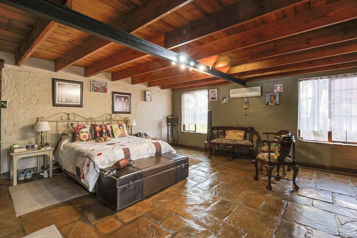 Spacious bedroom featuring rustic stone flooring, exposed timber ceiling beams, and textured walls, creating a warm and character-filled living space.