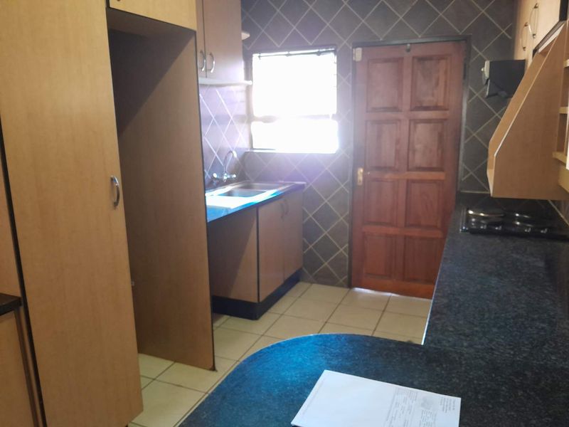 A functional kitchen featuring laminate cabinetry, granite countertops, a built-in hob, and tiled finishes, offering a practical layout for daily use.