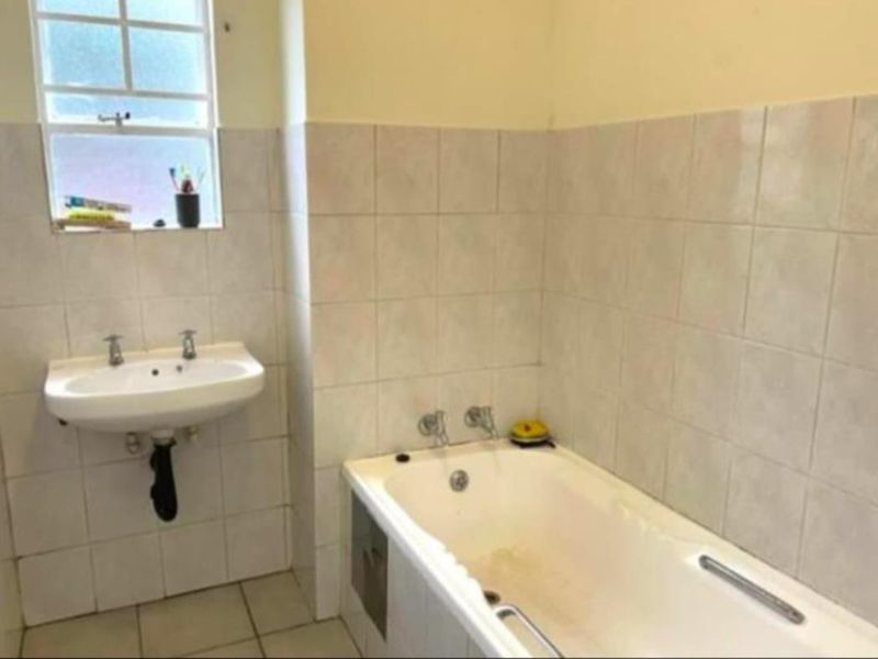 A functional bathroom featuring a built-in bathtub and wall-mounted basin, finished with neutral ceramic tiling throughout.