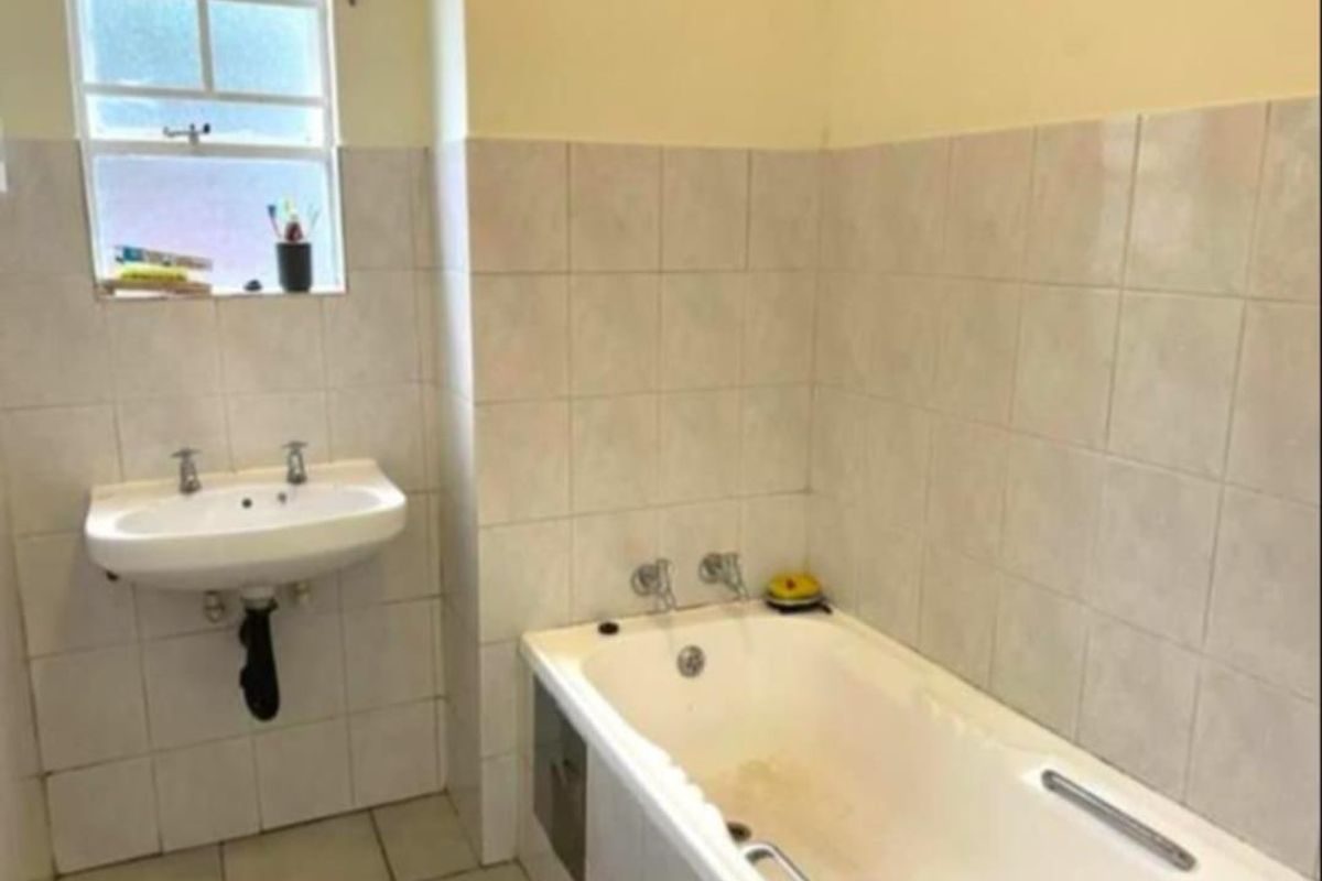 A functional bathroom featuring a built-in bathtub and wall-mounted basin, finished with neutral ceramic tiling throughout.
