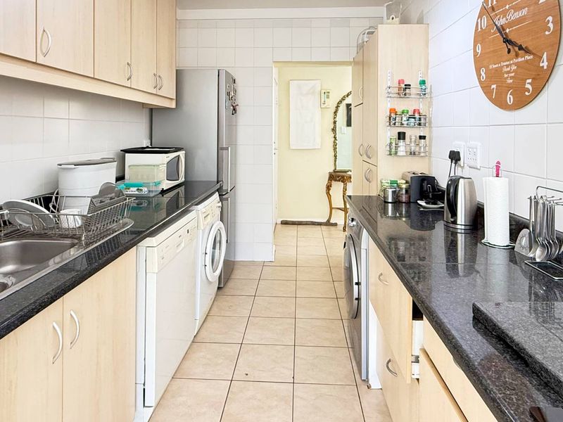 A functional galley-style kitchen featuring laminate cabinetry, granite countertops, tiled backsplash, and dedicated spaces for integrated laundry and kitchen appliances.
