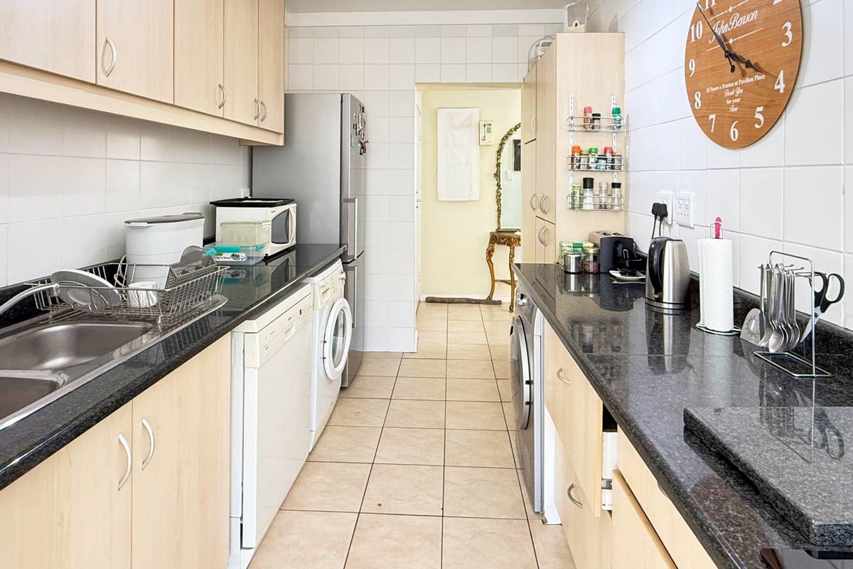 A functional galley-style kitchen featuring laminate cabinetry, granite countertops, tiled backsplash, and dedicated spaces for integrated laundry and kitchen appliances.