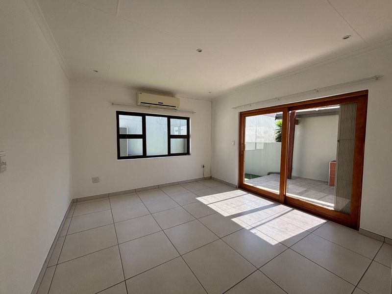 Bright and spacious living area featuring neutral tiled flooring, an air conditioning unit, and large sliding glass doors leading to an outdoor patio.