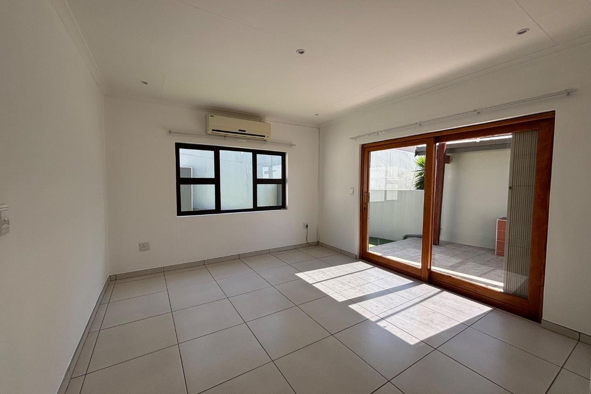 Bright and spacious living area featuring neutral tiled flooring, an air conditioning unit, and large sliding glass doors leading to an outdoor patio.