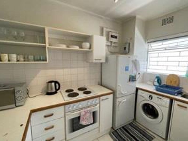 Compact kitchen featuring white cabinetry, electric hob, built-in oven, tiled backsplash, and integrated laundry plumbing, offering a functional layout for an apartment.