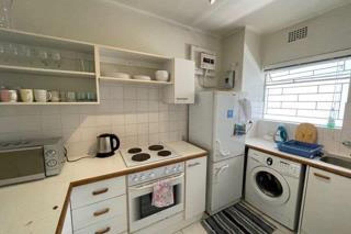Compact kitchen featuring white cabinetry, electric hob, built-in oven, tiled backsplash, and integrated laundry plumbing, offering a functional layout for an apartment.