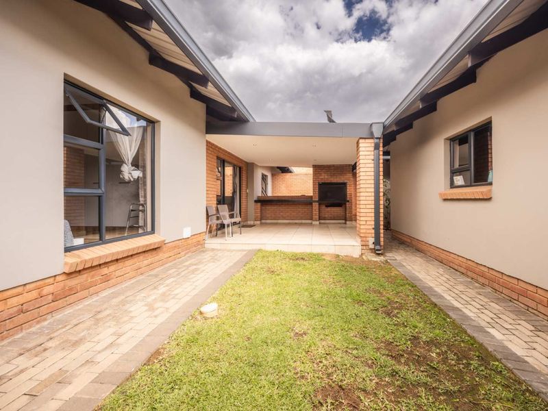 Covered patio area featuring a built-in braai, brick accents, and tiled flooring, overlooking a small garden courtyard.