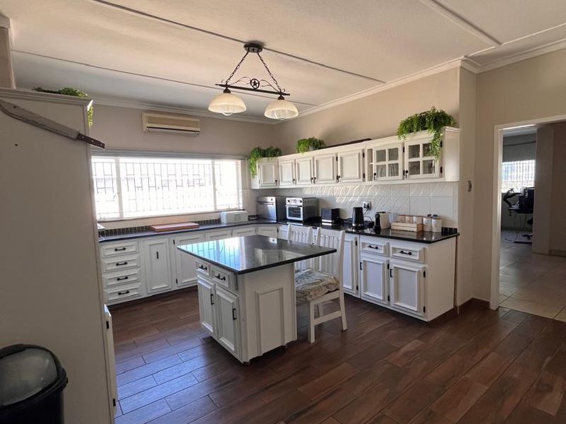 Spacious kitchen featuring white cabinetry, granite countertops, a central island, and wood-look tiled flooring, offering a functional and well-maintained cooking space.