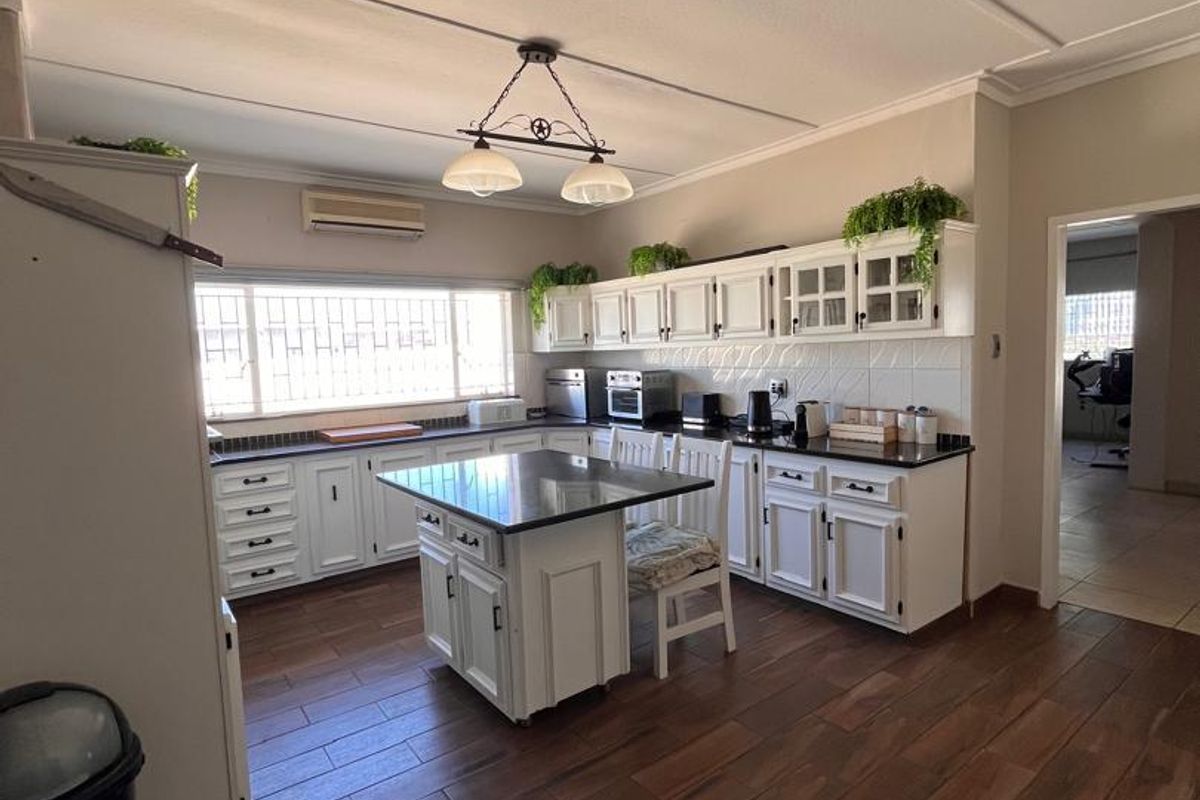 Spacious kitchen featuring white cabinetry, granite countertops, a central island, and wood-look tiled flooring, offering a functional and well-maintained cooking space.