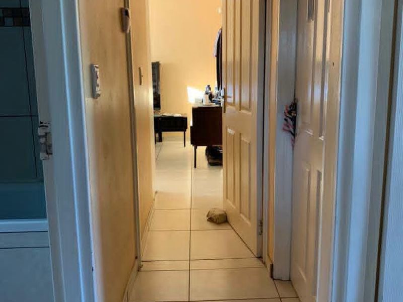 A narrow residential hallway with tiled flooring connecting multiple rooms, showing signs of wear and dated wall finishes.