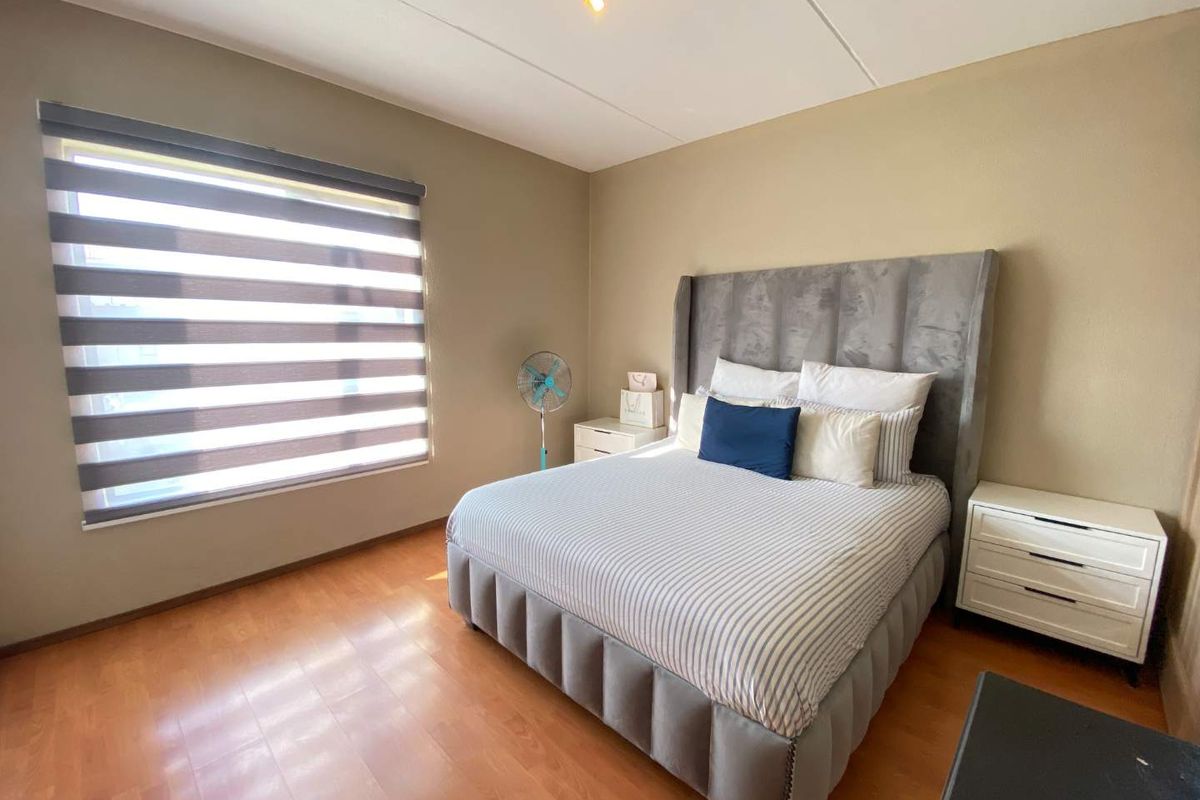 A well-maintained bedroom featuring warm-toned laminate flooring, neutral wall finishes, and modern zebra-style window blinds.