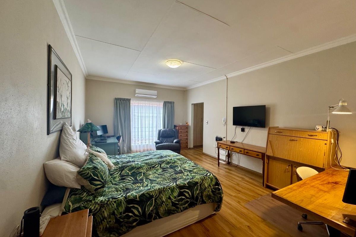 Spacious bedroom featuring laminate flooring, air conditioning, and neutral wall finishes, offering a comfortable and functional living space.