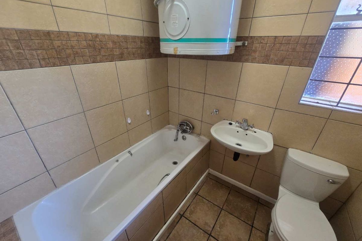 A functional bathroom featuring a bathtub, wall-mounted basin, toilet, and an electric water heater, finished with neutral wall and floor tiling.