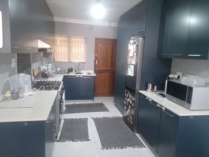Modern kitchen featuring dark blue cabinetry, stone countertops, gas hob, extractor fan, and tiled backsplash with neutral floor tiles.