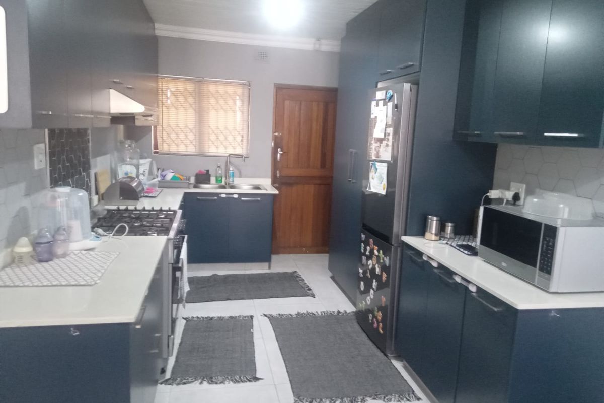 Modern kitchen featuring dark blue cabinetry, stone countertops, gas hob, extractor fan, and tiled backsplash with neutral floor tiles.