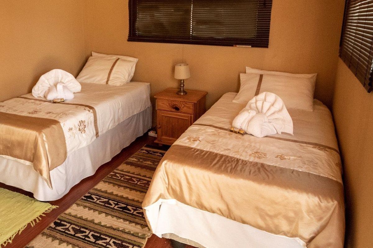 A compact bedroom featuring twin beds and horizontal window blinds, providing a functional sleeping space.