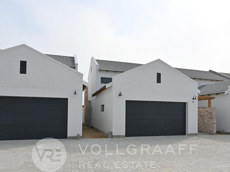 A view of the modern townhouse complex featuring white brick facades, tiled roofs, and multiple double garages with paved driveway access.