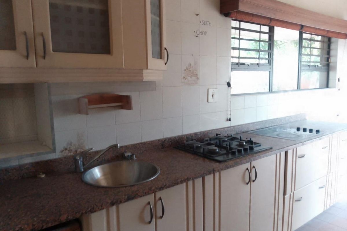 A dated kitchen featuring granite countertops, built-in gas hob, stainless steel sink, and light-toned cabinetry with ample storage space.