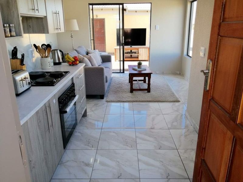 An open-plan living and kitchen area featuring modern marble-look floor tiles, contemporary cabinetry, and a sliding door leading to an outdoor patio space.